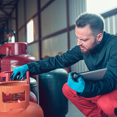 Male worker examining cylinders with digital tablet in liquified gas storage